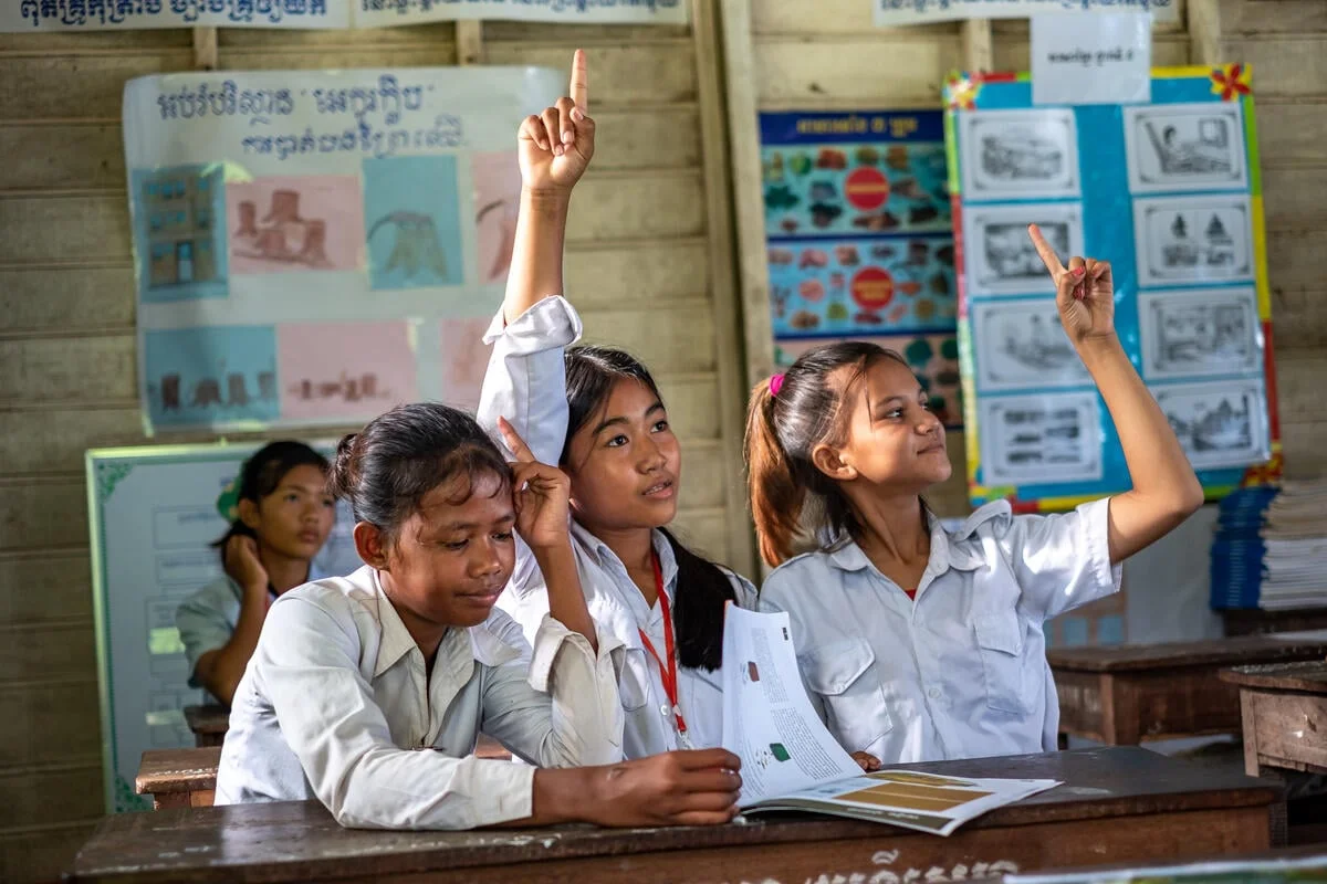 Cambodjaanse schoolmeisjes steken hun hand op in de klas